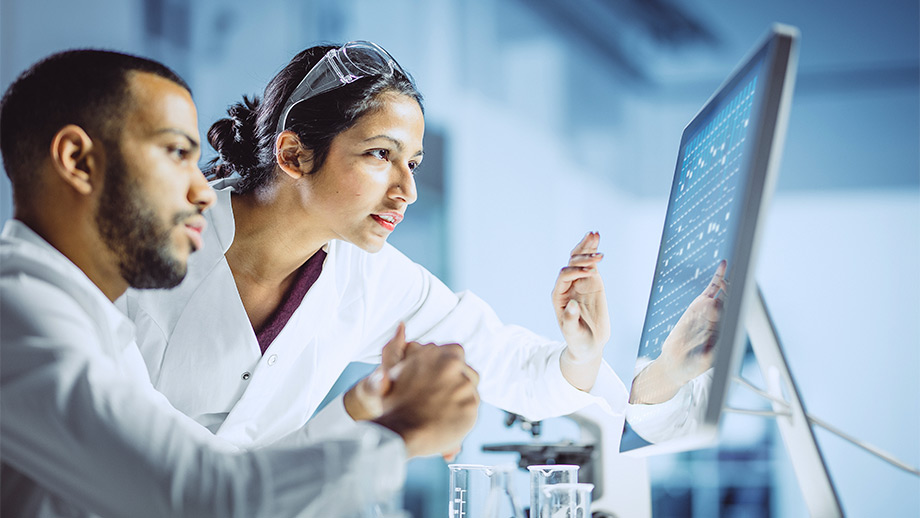 Two scientists in lab coats at a computer discussing their findings